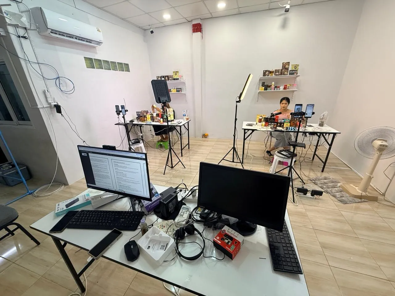 PAN's live-selling studio: a presenter at a product table under studio lights, phones on tripods streaming to Shopee and Lazada